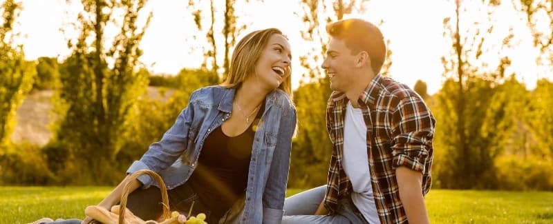 A couple smiling while sitting on the green grass having a picnic