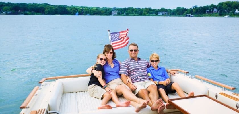 A family sits together on a boat with an American flag behind them, relaxing on the water during a sunny day.