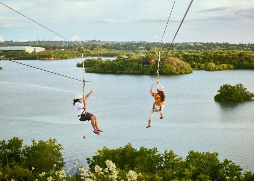 Two riders soar over a lake on a zip line during an adventure outing near the Poconos.