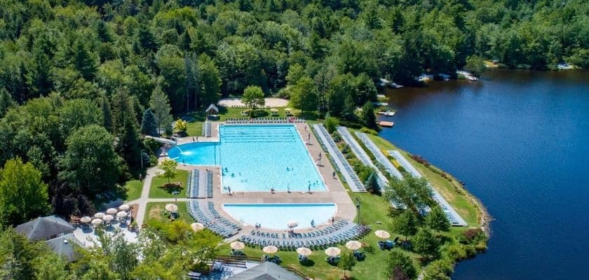 large outdoor swimming pool at lake naomi club surrounded by lounge chairs umbrellas and dense green forest next to a peaceful lake