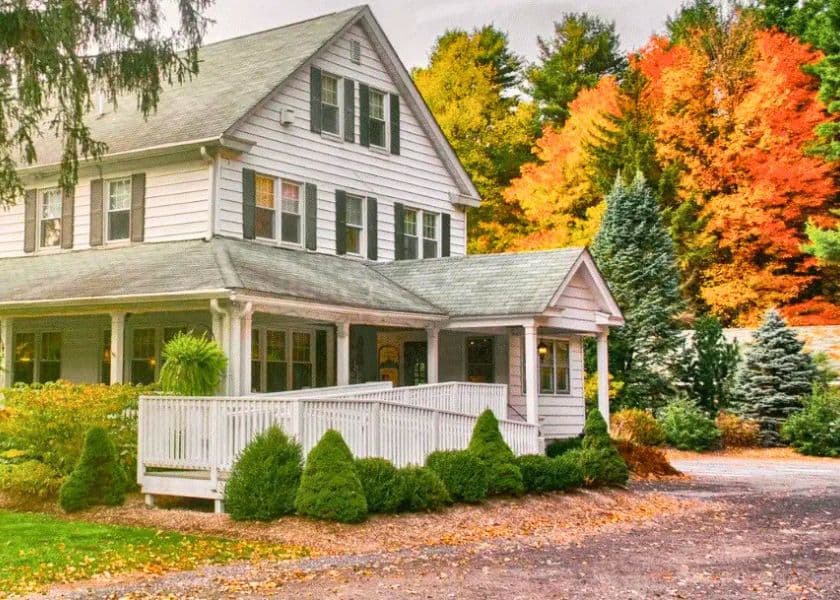 The Mountaintop Lodge porch and exterior, a white farmhouse style building surrounded by trees in autumn color.