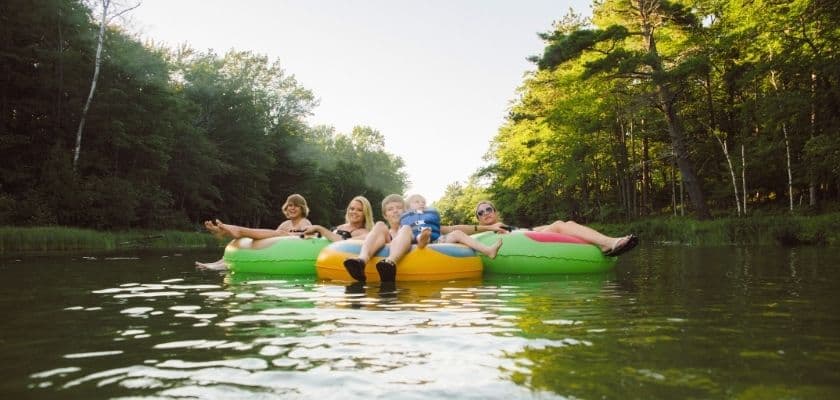 A group of people floats down a river in colorful tubes, relaxing on the water amid trees.