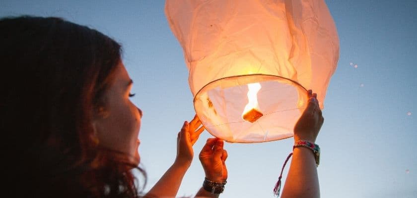 woman releasing glowing lantern into the evening sky at fall lantern festival