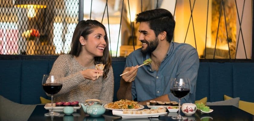 couple smiling at each other eating dinner with a glass of wine in front of them
