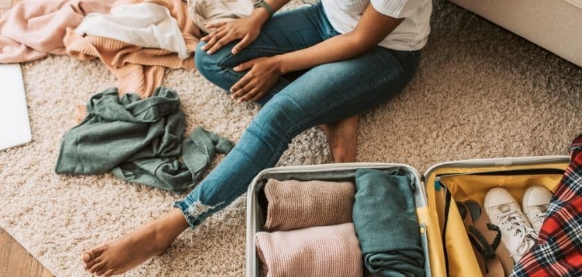 person packing a suitcase on the floor with folded clothes and shoes nearby
