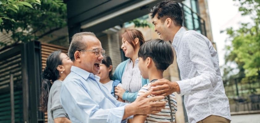 joyful family reunion smiling laughing and hugging outside near a house with greenery in the background